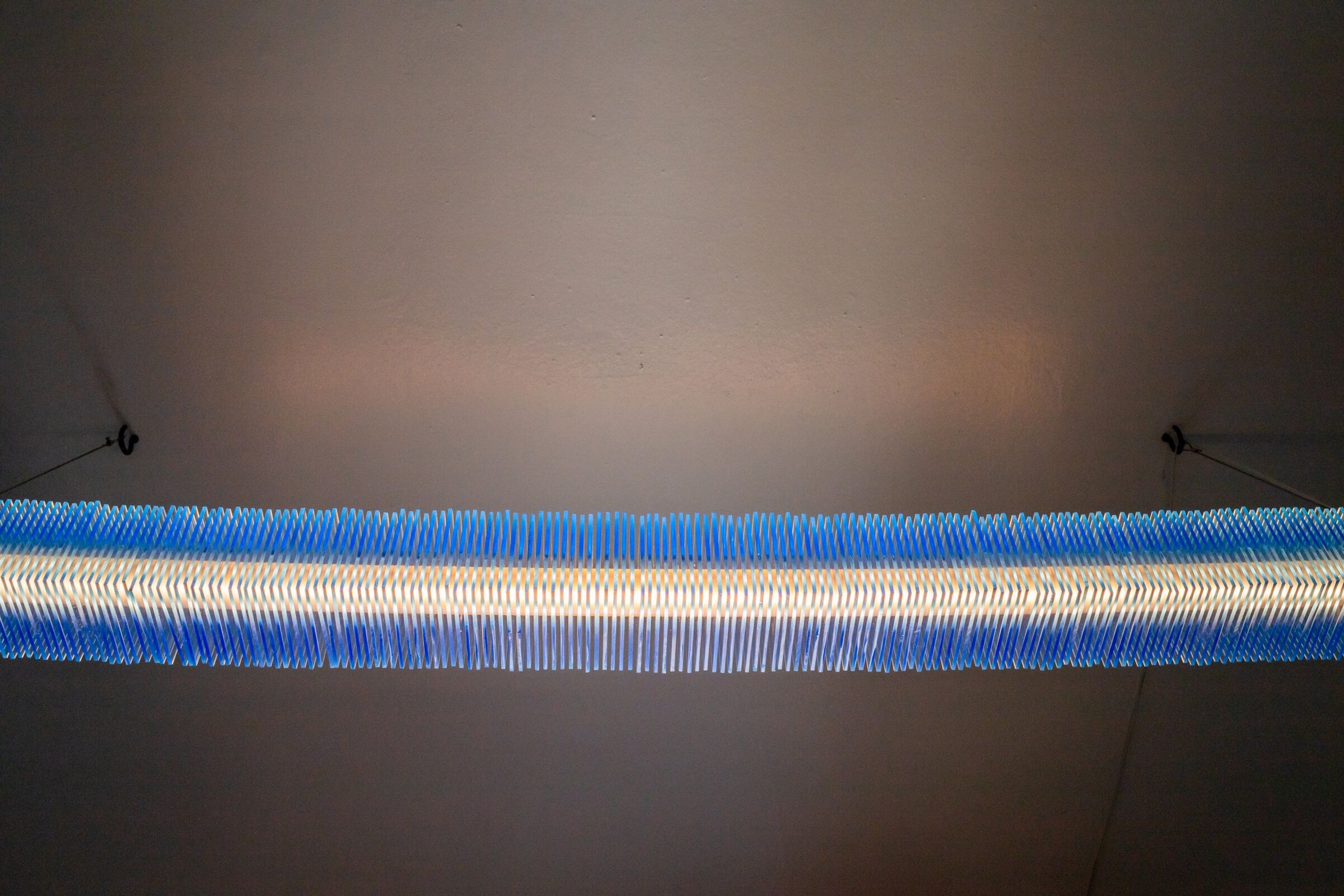 Radiator I viewed from directly underneath: a blue horizontal bar with a bright warm core down its center, casting a soft halo on the ceiling above