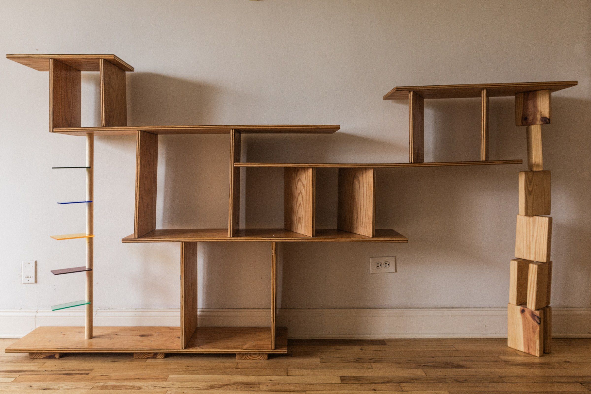 The wooden shelving unit at an angle, open compartments stacked with books and objects, warm light low in the frame.