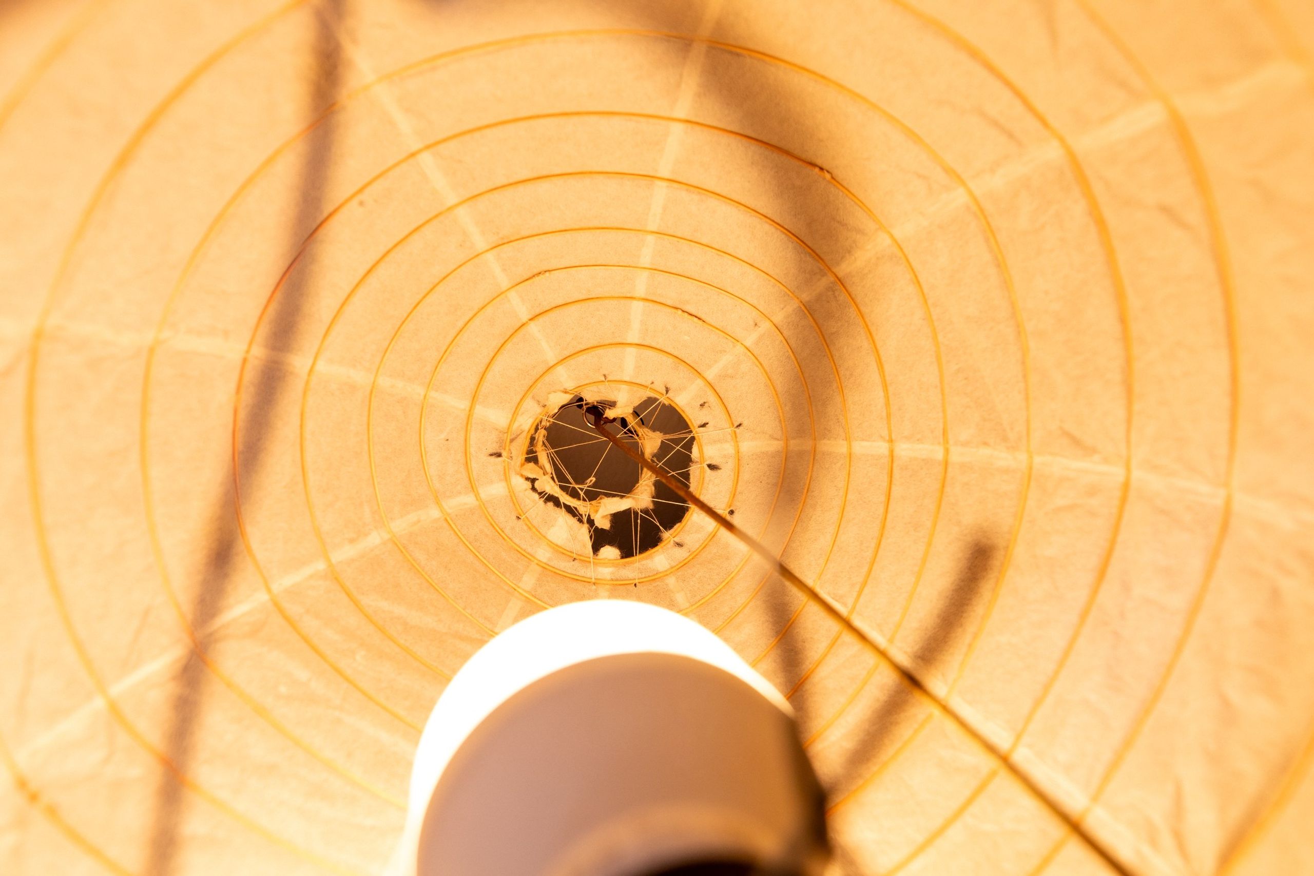 Close view of the mended seam crossing the lantern's ribs, dark repair against warm paper.