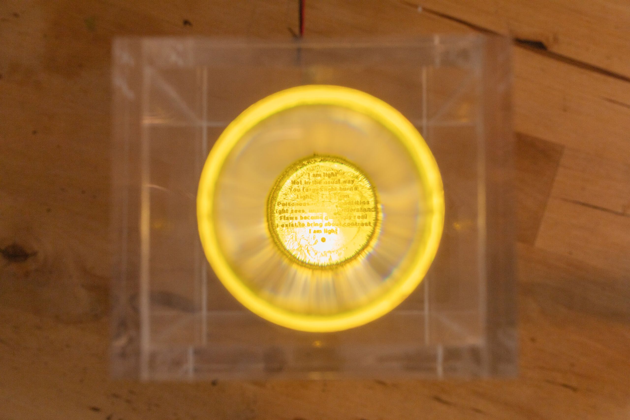 Direct top-down view through the lens of internal artifact: the printed poem now legible inside the warm yellow halo, suspended at the center of the lens