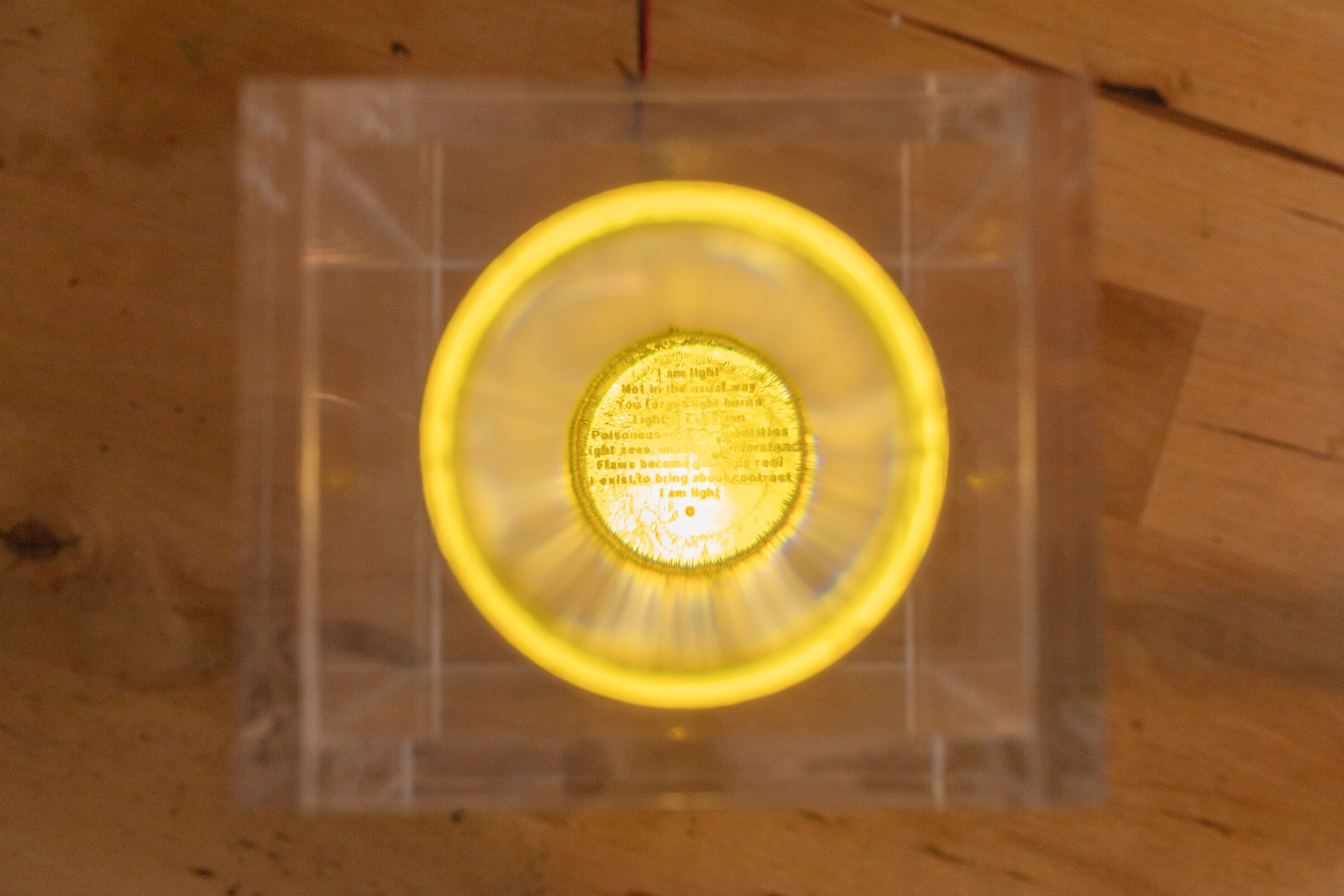 Direct top-down view through the lens of internal artifact: the printed poem now legible inside the warm yellow halo, suspended at the center of the lens