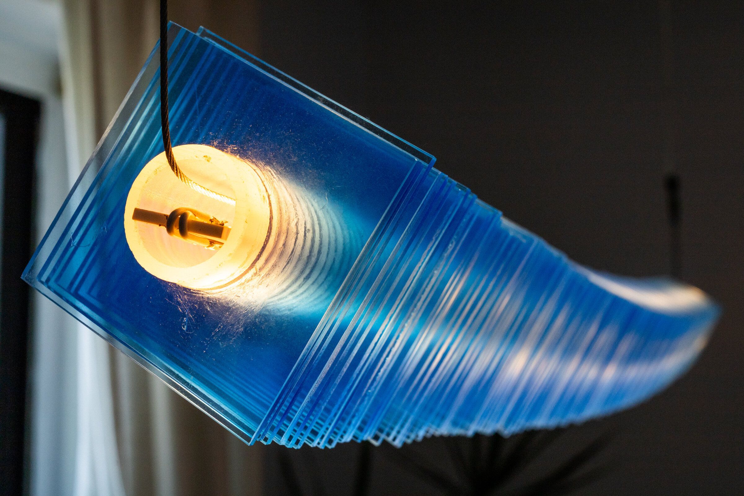 End view of radiator I from below: the Edison bulb and ceramic socket visible inside the stack of blue acrylic plates, light radiating outward through the layers