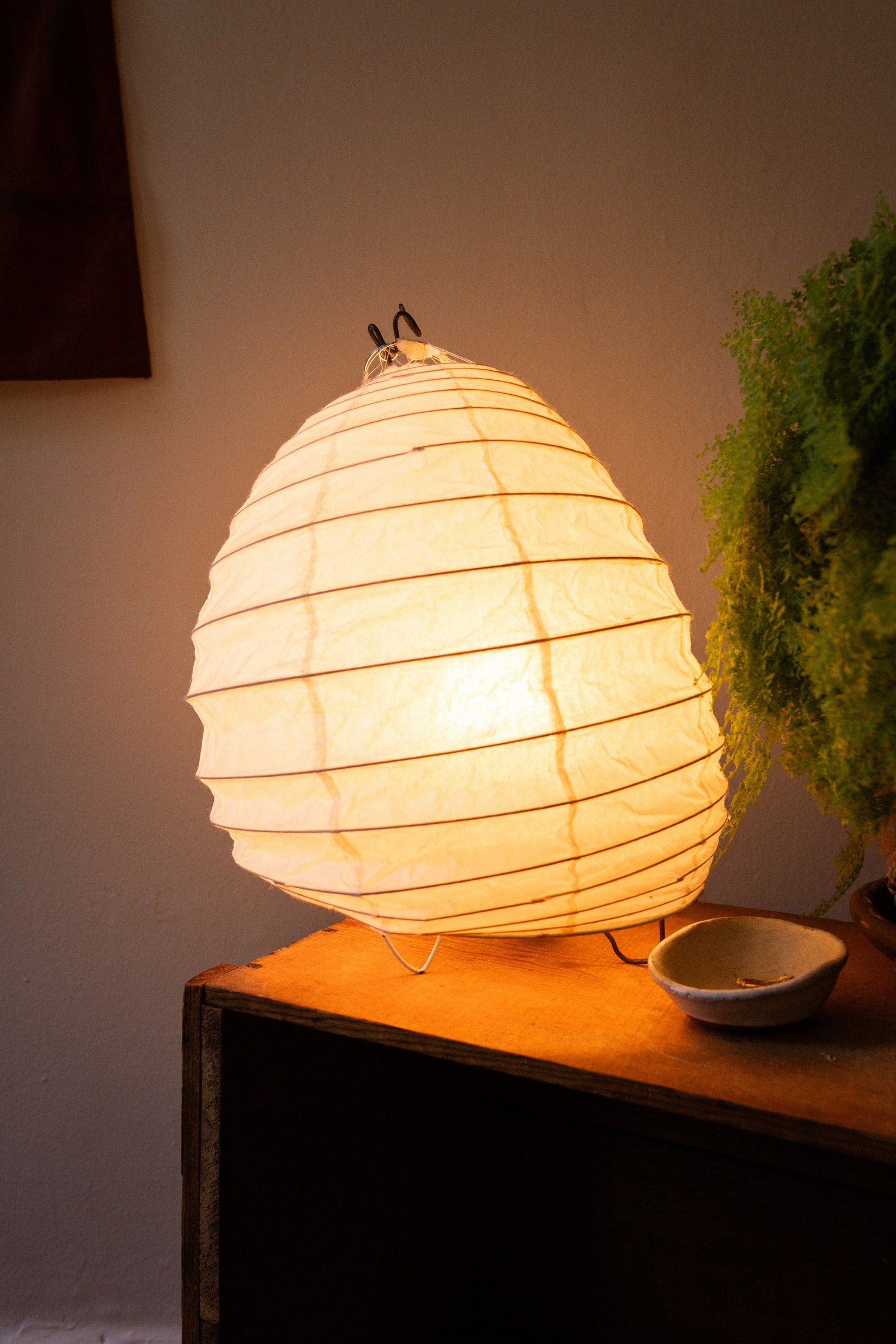 A round paper Akari lantern lit from within, glowing warm in a dim room.