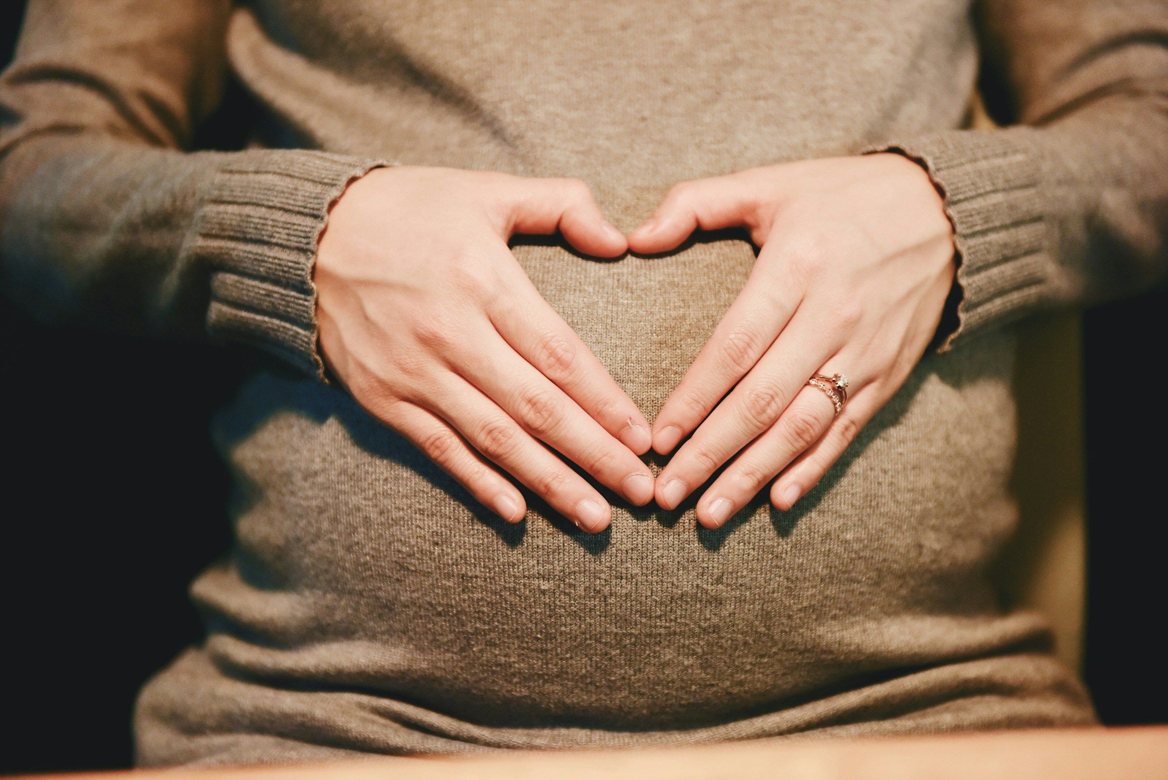 Schwangere Frau formt mit den Händen ein Herz auf ihrem Bauch