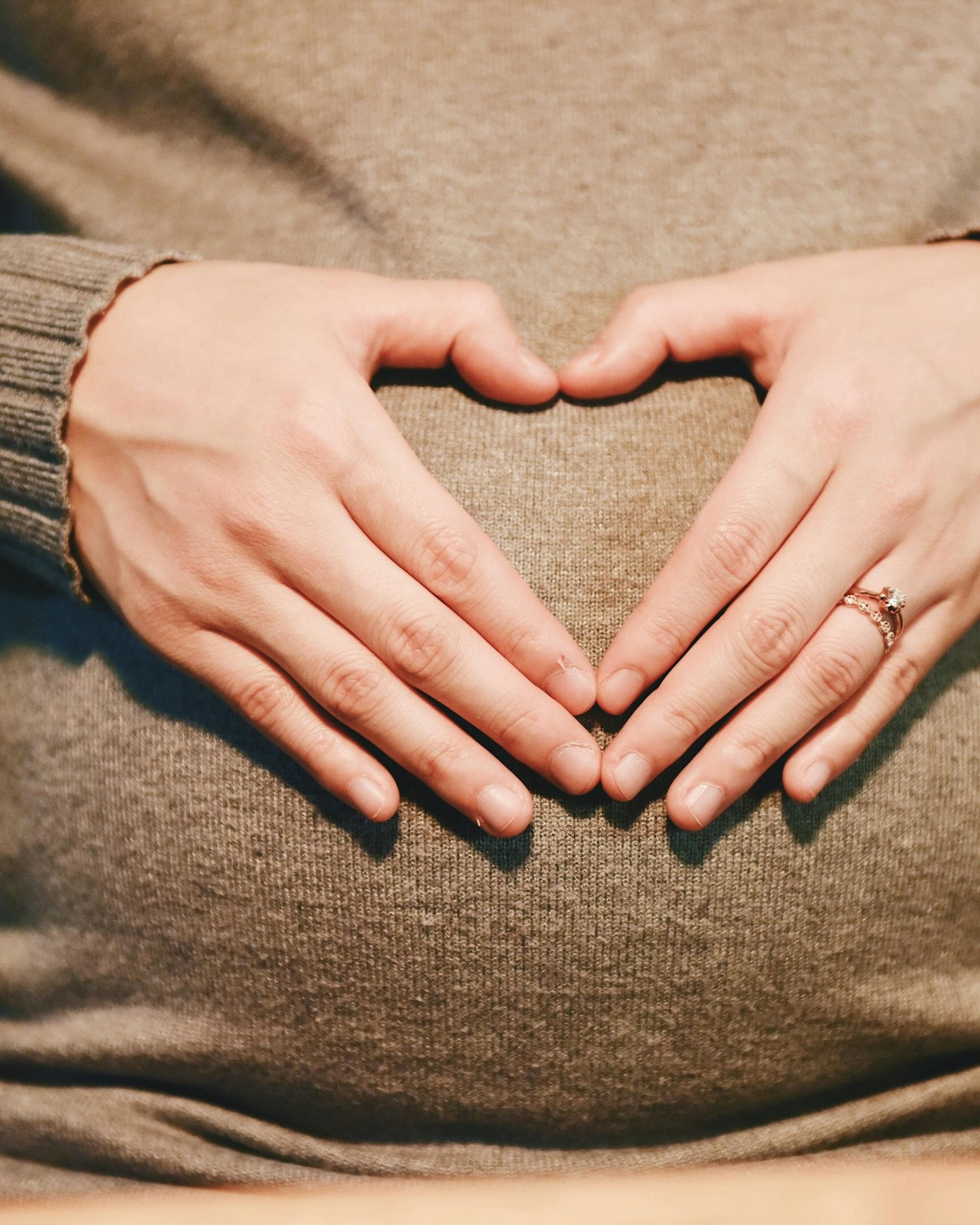Schwangere Frau formt mit den Händen ein Herz auf ihrem Bauch