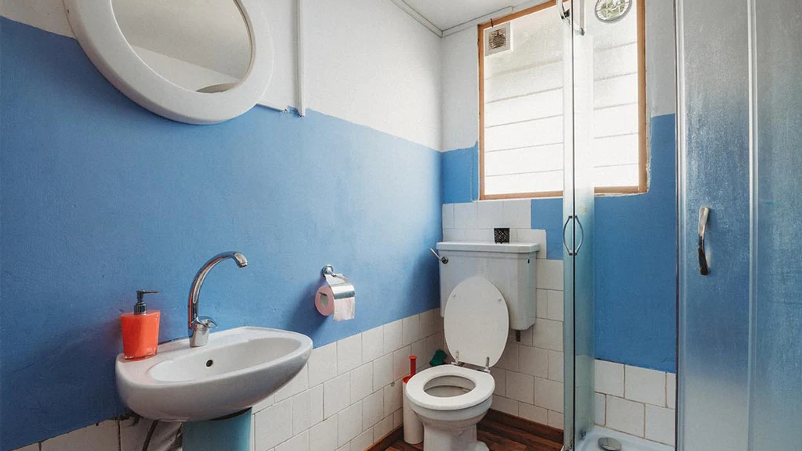 a bathroom with a toilet, sink and glass shower cubicle, with blue walls