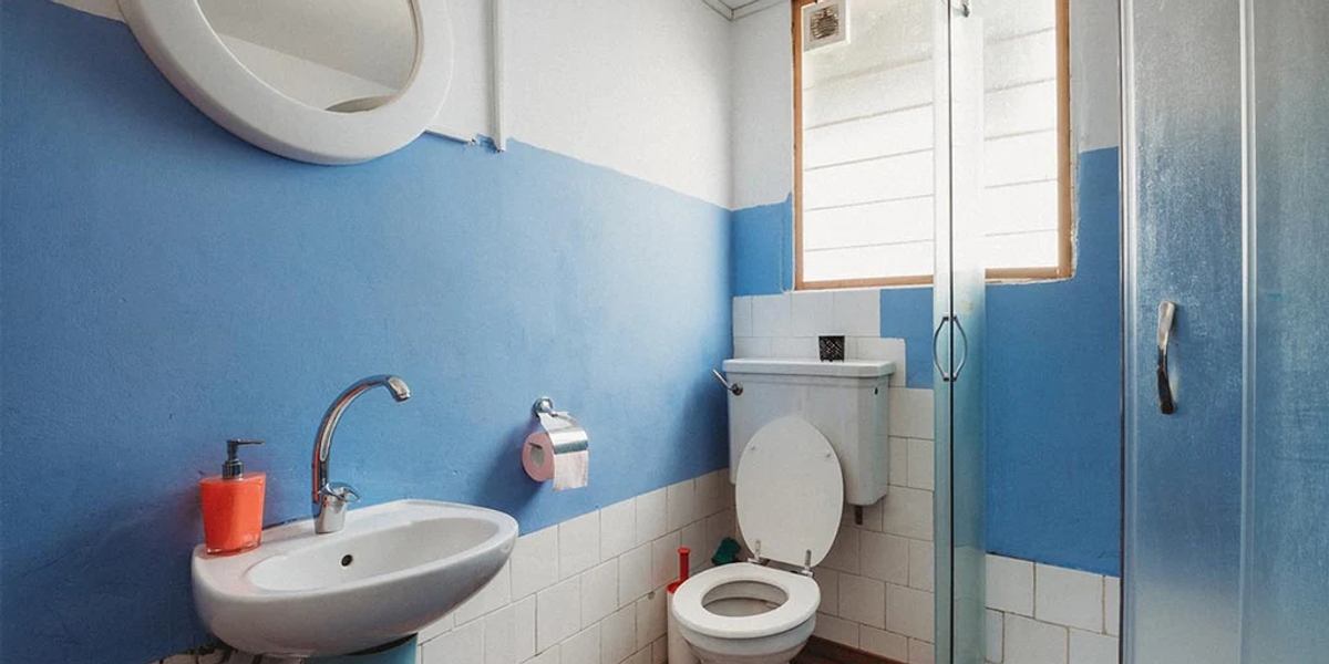 a bathroom with a toilet, sink and glass shower cubicle, with blue walls
