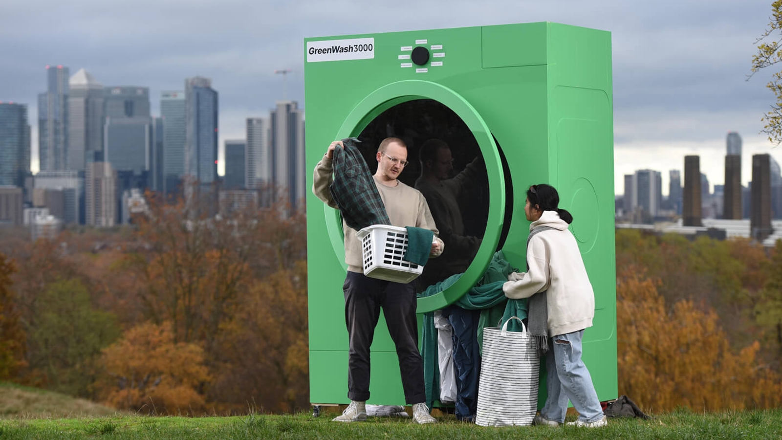 A man taking clothes out of a washing basket in front of a big green washing machine