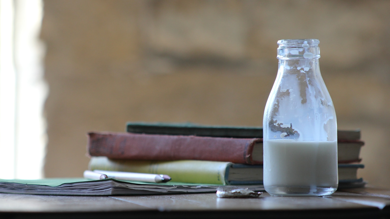 A glass bottle of milk on a table next to a stack of books