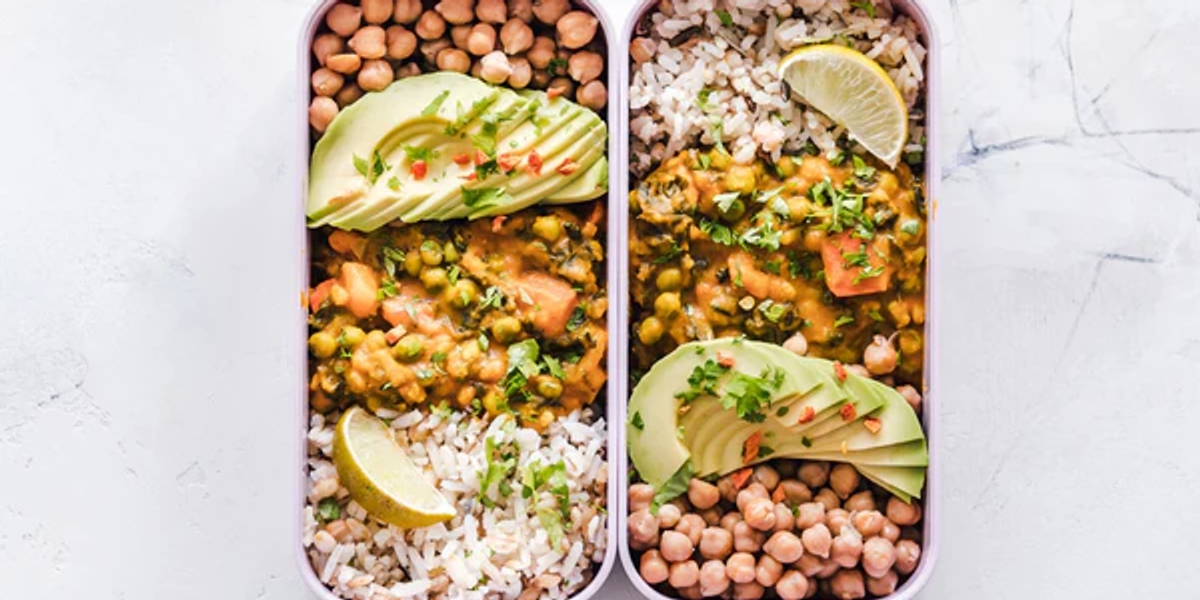 Two open lunchboxes on a counter with rice, chickpeas and avocado