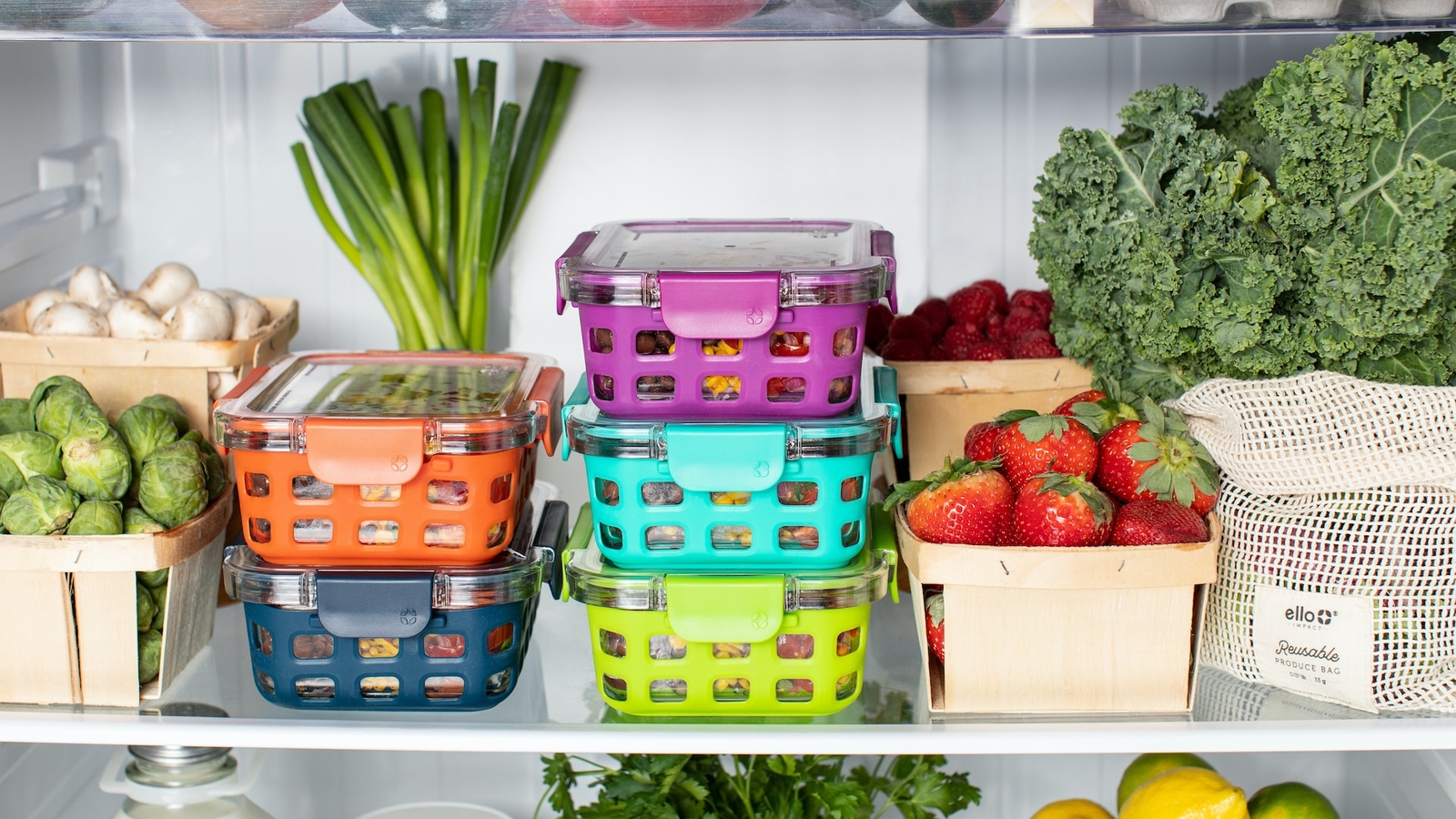 A well-organized refrigerator interior with colorful, stacked food storage containers, fresh fruits in wooden crates, and leafy greens.