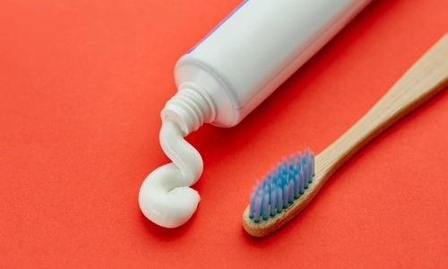 A white tube of toothpaste next to a bamboo toothbrush on a red background