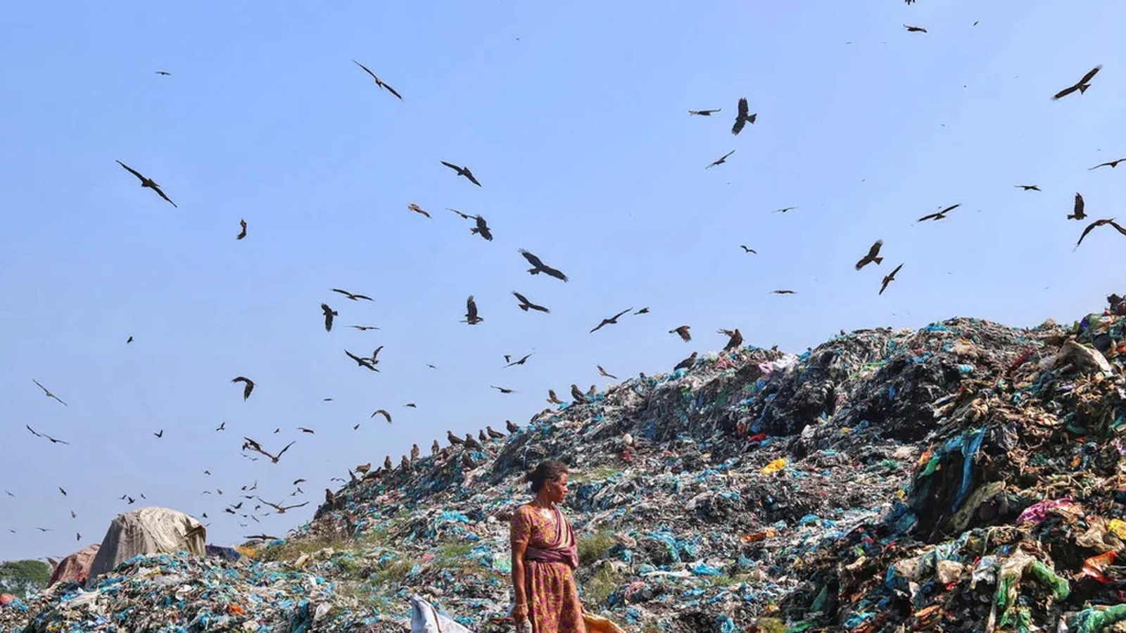 A photo of a rubbish tip filled with textile waste with birds flying above against a blue sky