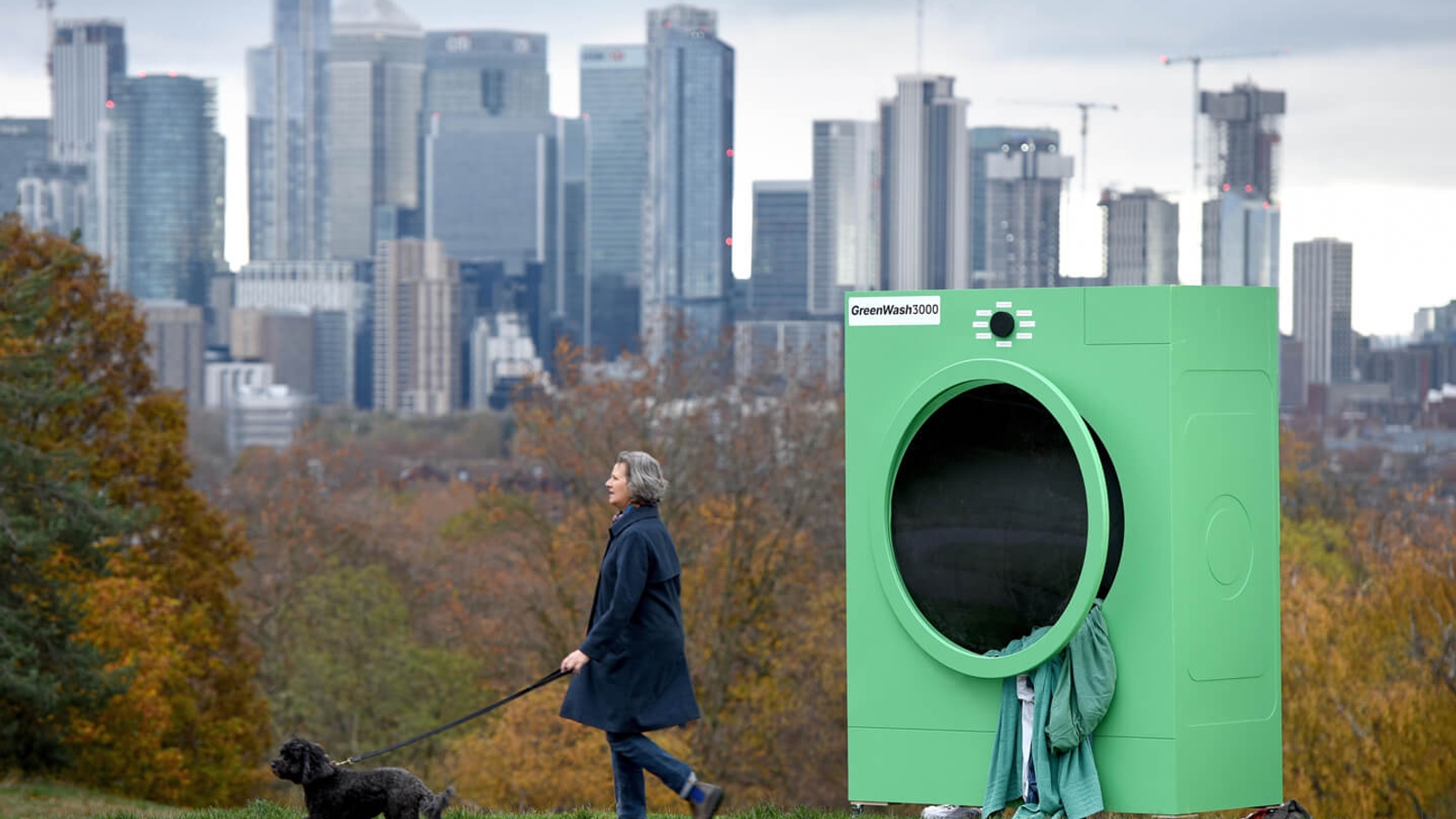 A woman walking her dog in front of a big green washing machine