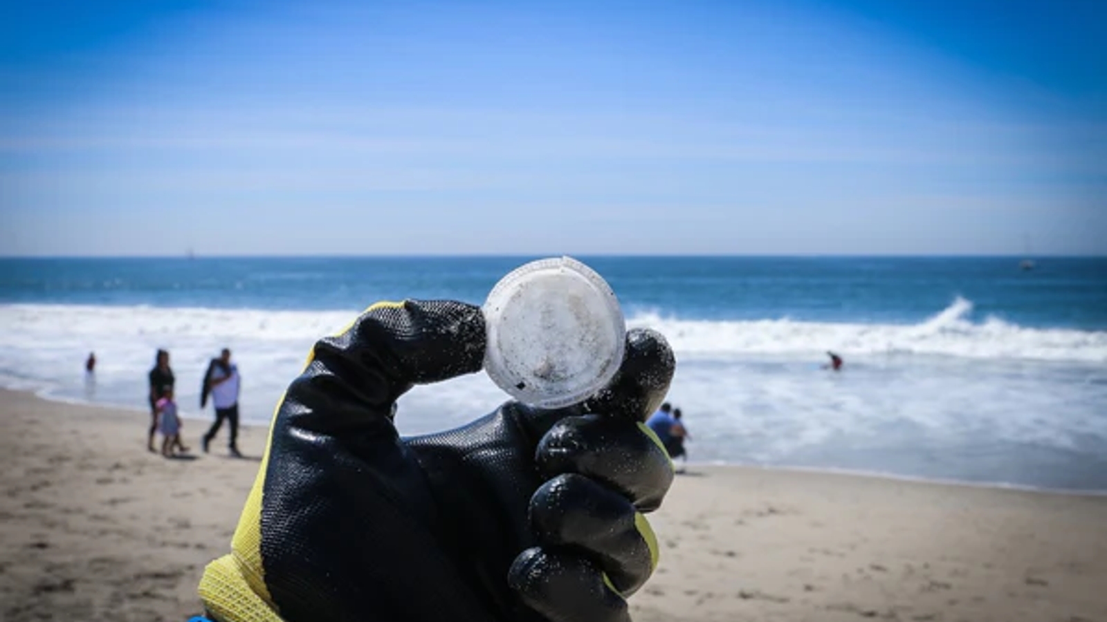 someone's gloved hand holding up a plastic bottle cap on a beach