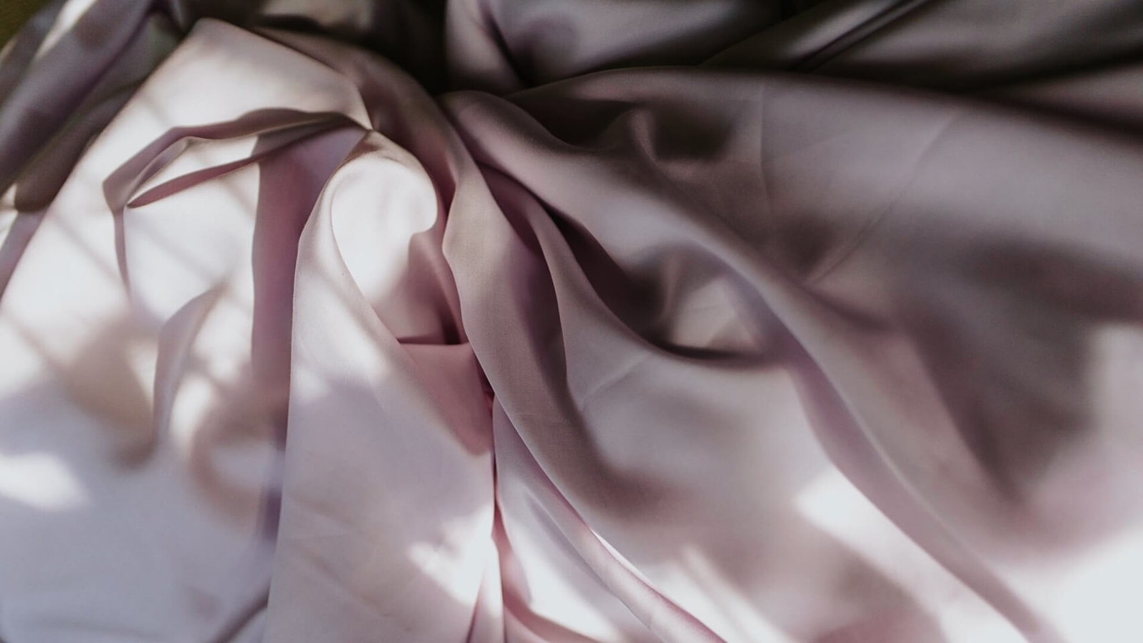 Close-up of smooth, pink fabric with soft folds, illuminated by natural light creating shadows