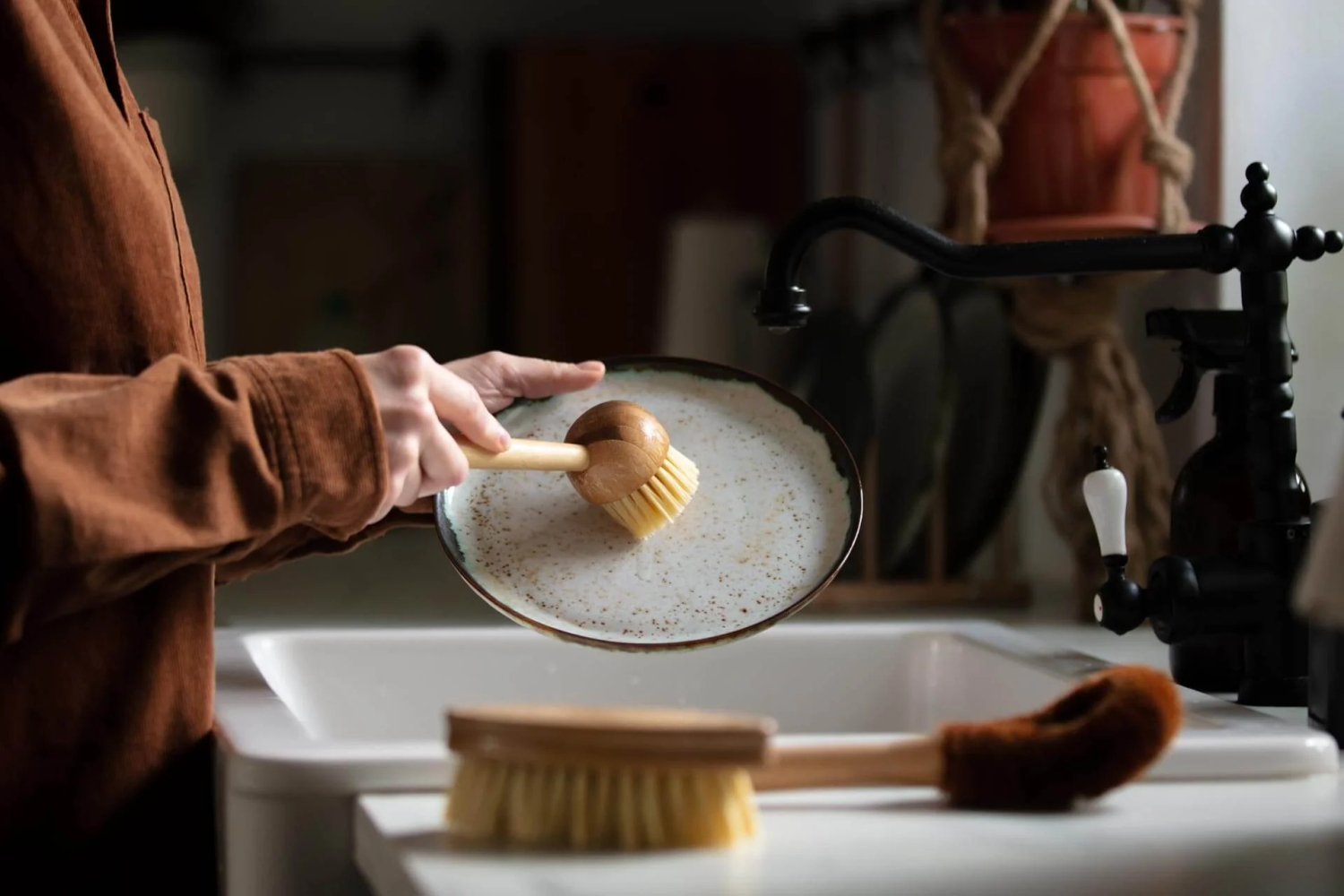 Washing a plate on top of a sink using a wooden brush