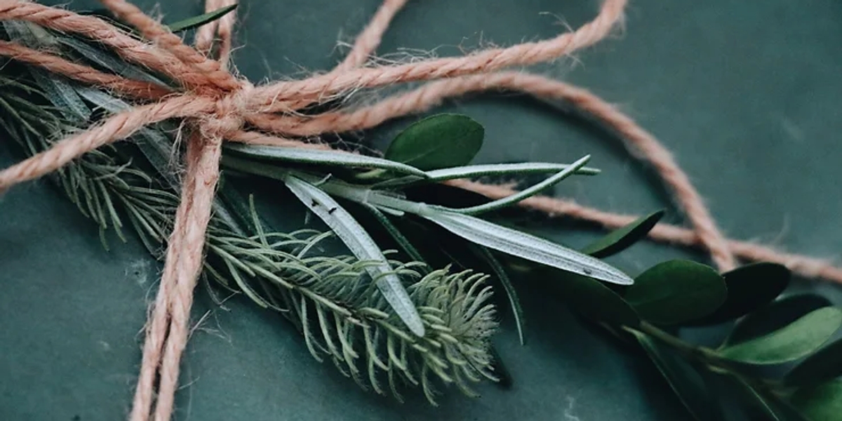 A bow tied with natural string, with herbs and evergreen sprigs tied underneath