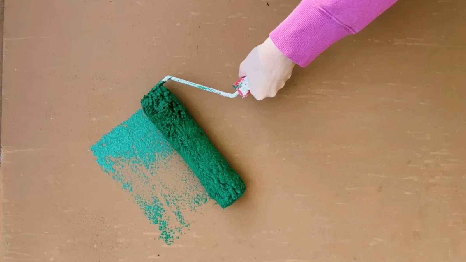 A paint roller with green paint being painted onto a wooden board by a hand