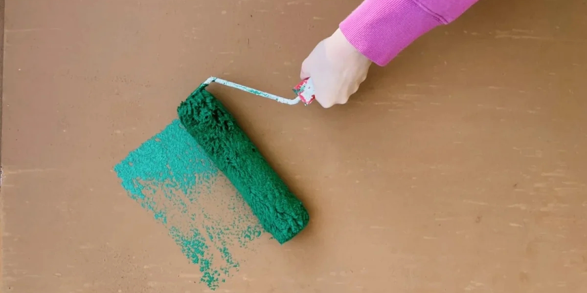 A paint roller with green paint being painted onto a wooden board by a hand