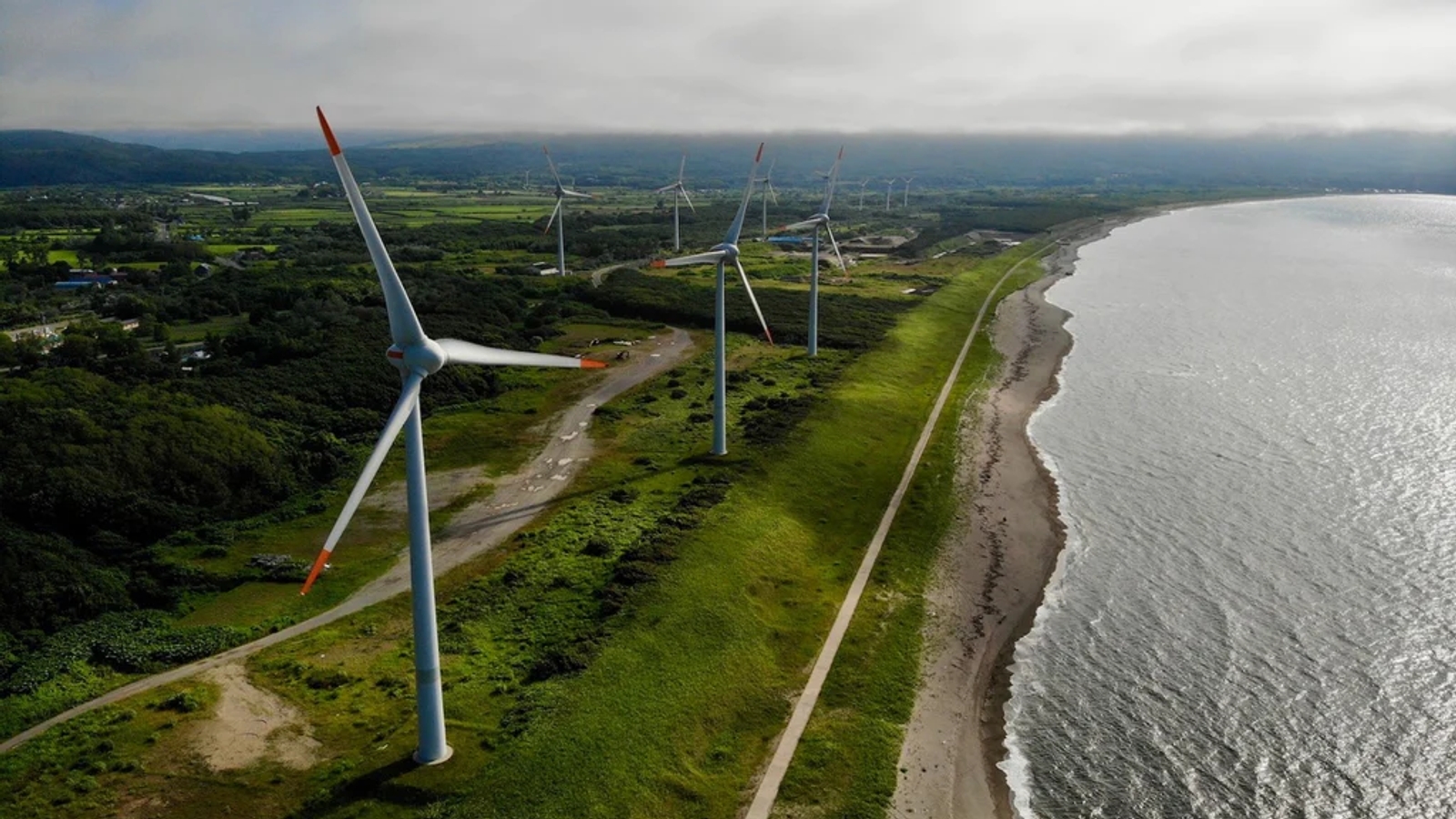 A photo of a row of wind turbines on the shore next to a beach