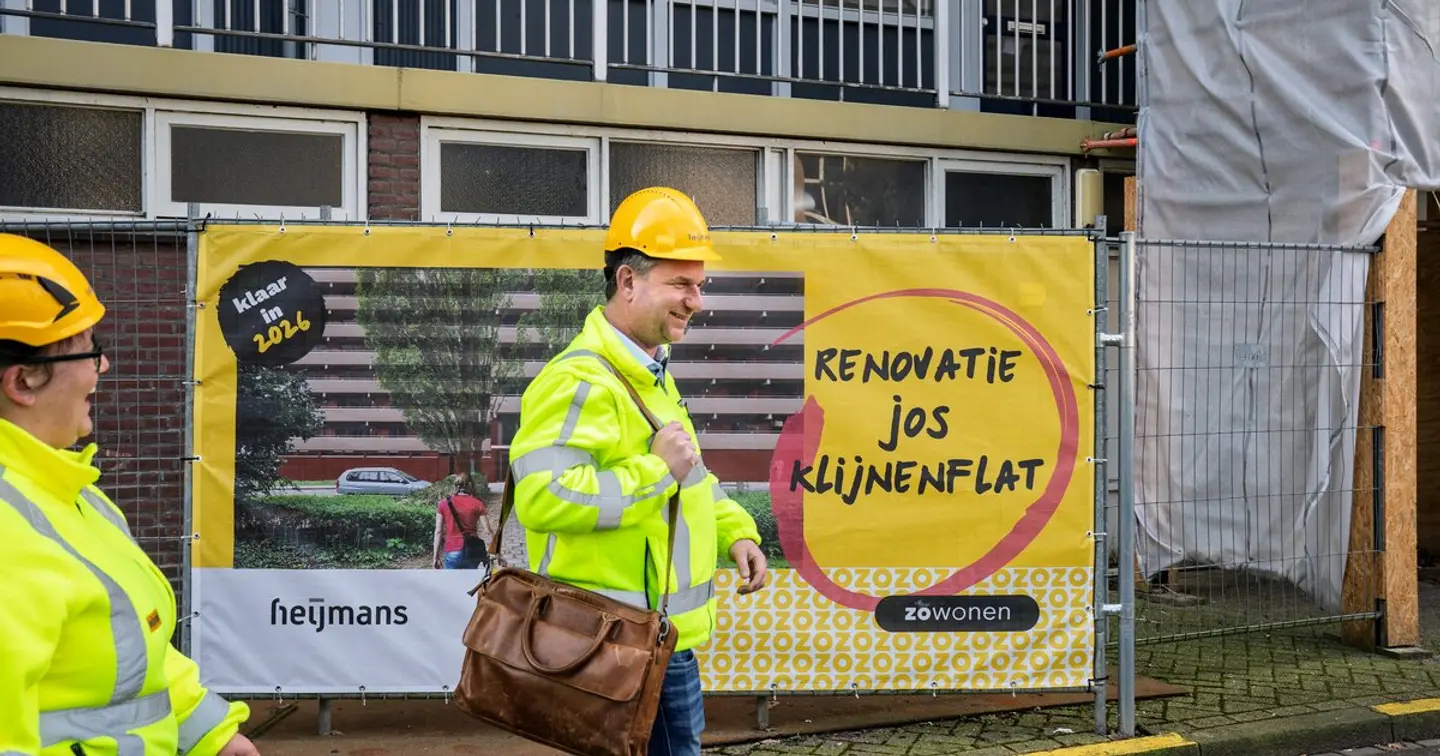 Heijmans-projectmanager bij het bouwhek met spandoek 'Renovatie Jos Klijnenflat' in Geleen-Zuid, in opdracht van woningcorporatie ZOwonen