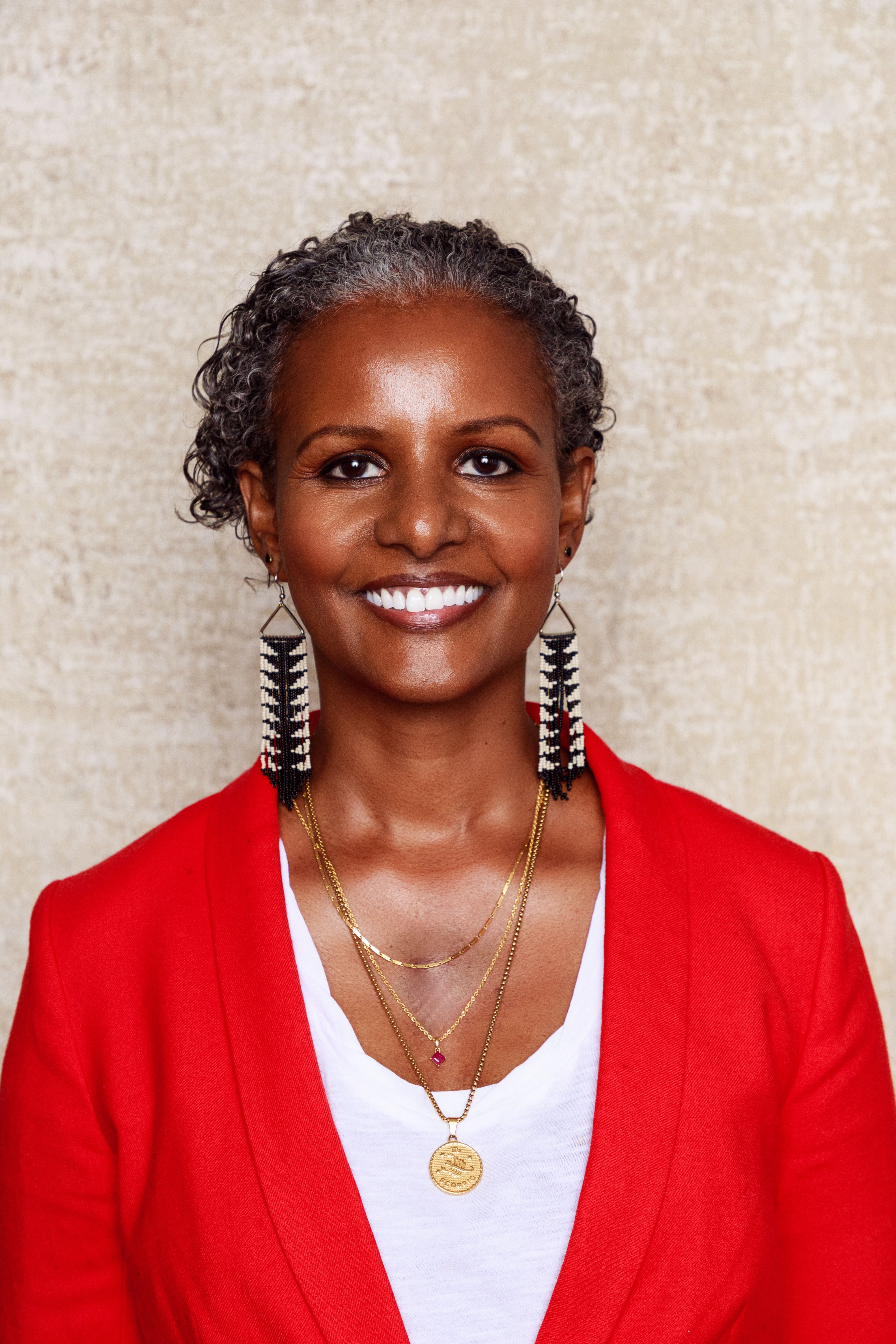 Sebene Selassie headshot wearing a red jacket and beaded earrings with a black and white chevron motif
