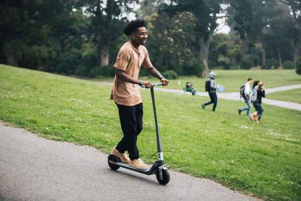 Young male riding electric scooter park