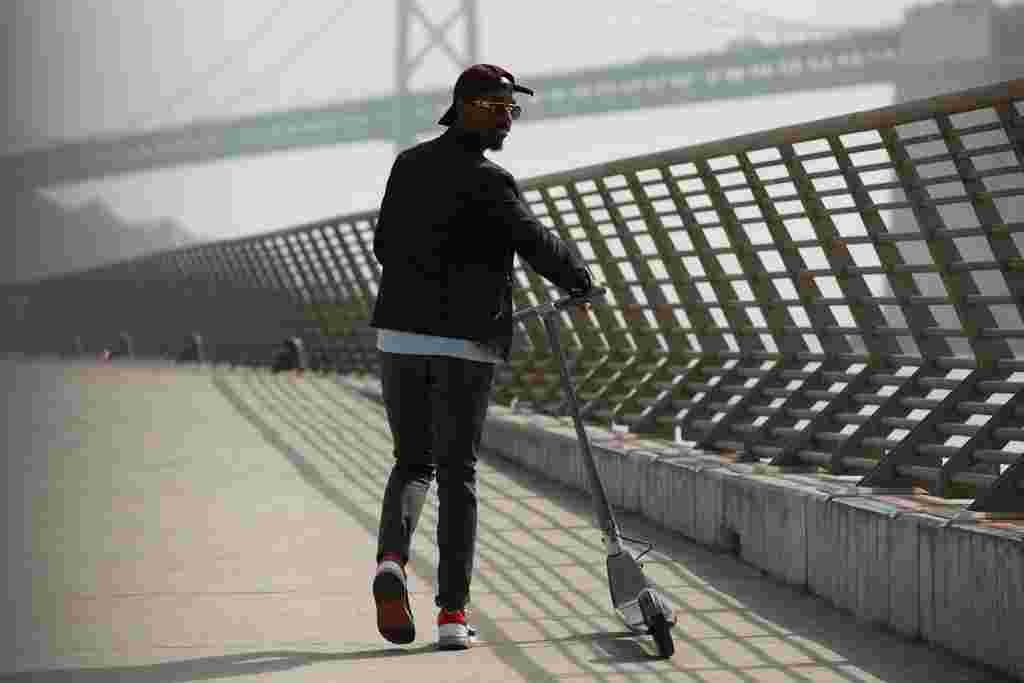 Man walking with scooter on bridge