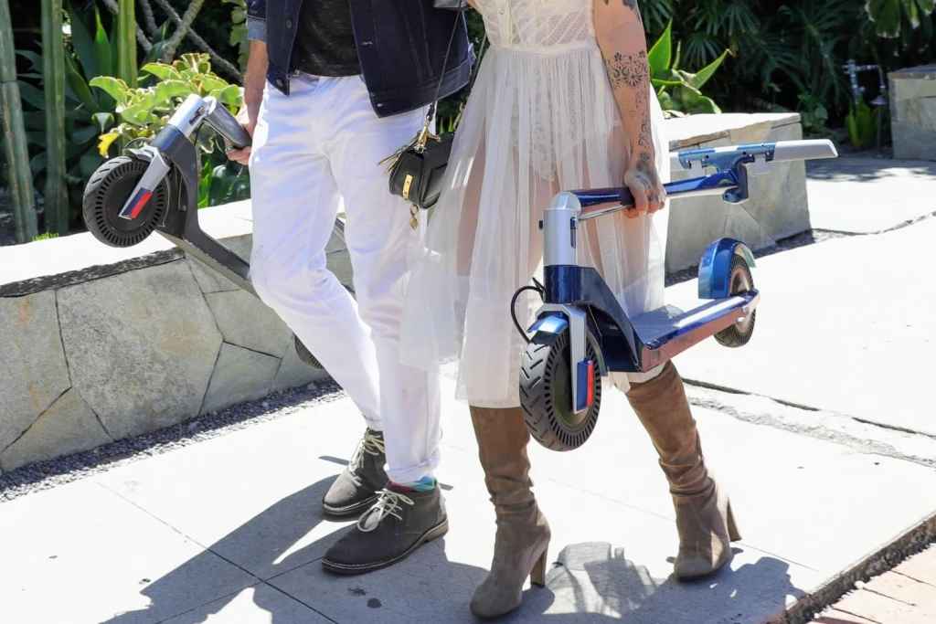2 people carrying folded electric scooters
