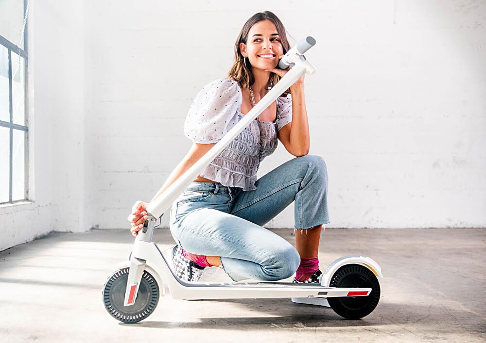 Young woman kneeling with e-scooter