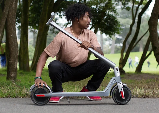 Man in park squatting down next to foldable electric scooter