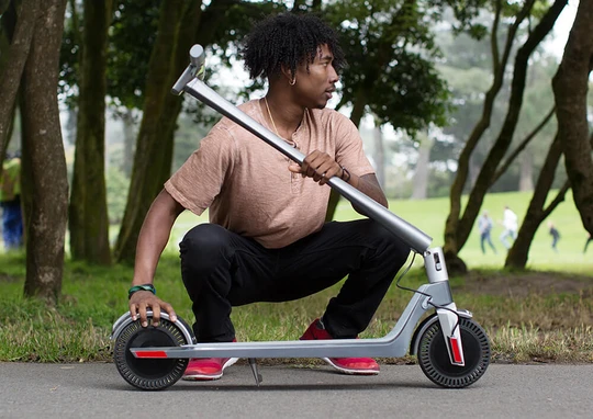 Hombre en el parque en cuclillas junto a patinete eléctrico plegable