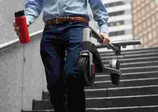 Man carrying a coffee and folded e-scooter down stairs