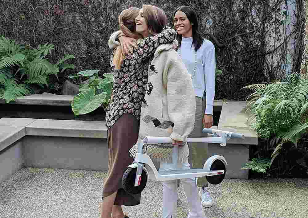 Woman embracing a friend while holding her folded e-scooter