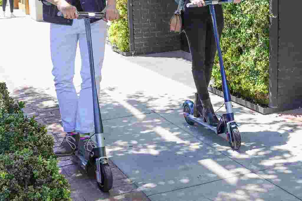 two unagi electric scooters riding on sidewalk