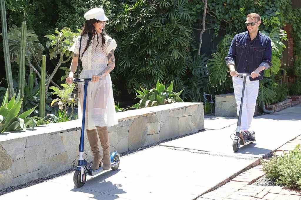 two people riding unagi e scooters on sidewalk