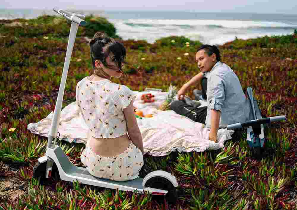 Jeune couple ayant un pique-nique au bord de l'océan avec leurs trottinette Unagi