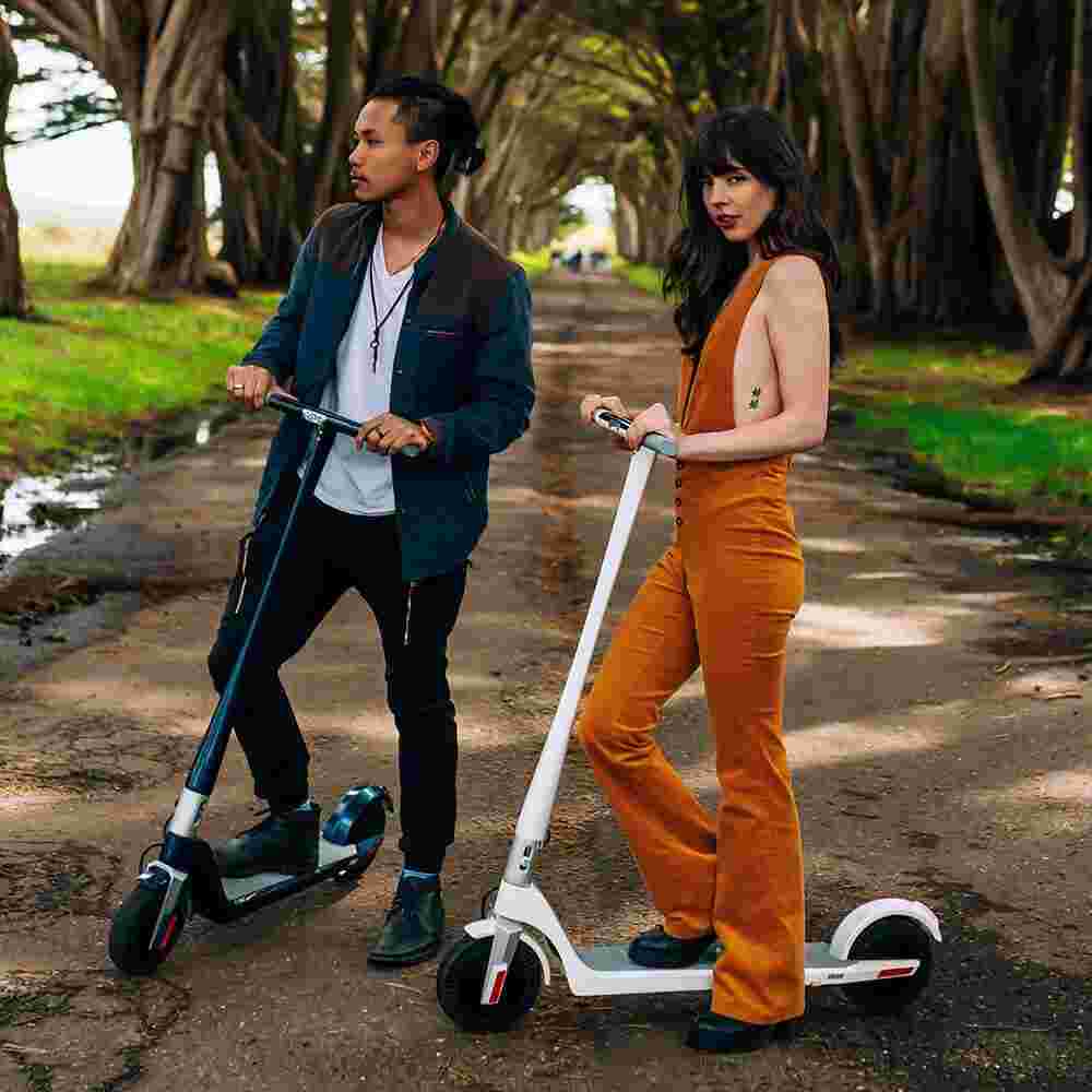 Couple à la mode dans le parc debout avec des trottinette électrique
