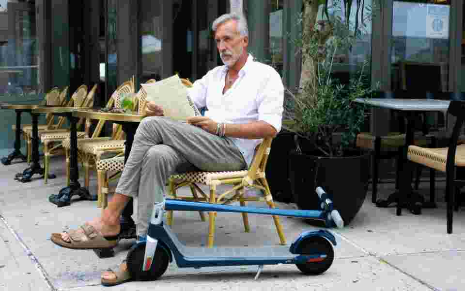 Grey haired man sitting outside cafe with electric scooter