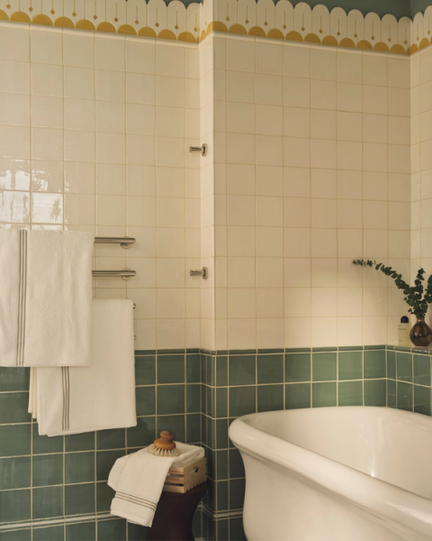 Children’s bathroom featuring playful green and cream tiles, scalloped yellow border detail, a classic freestanding tub and soft striped towels for a fresh, cheerful feel.