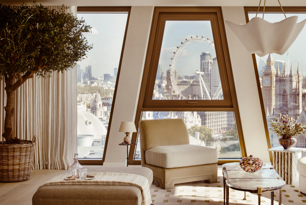 Living room corner in Westminster penthouse with sculptural coffee table, neutral armchair and geometric window framing views of the London Eye and Big Ben.
