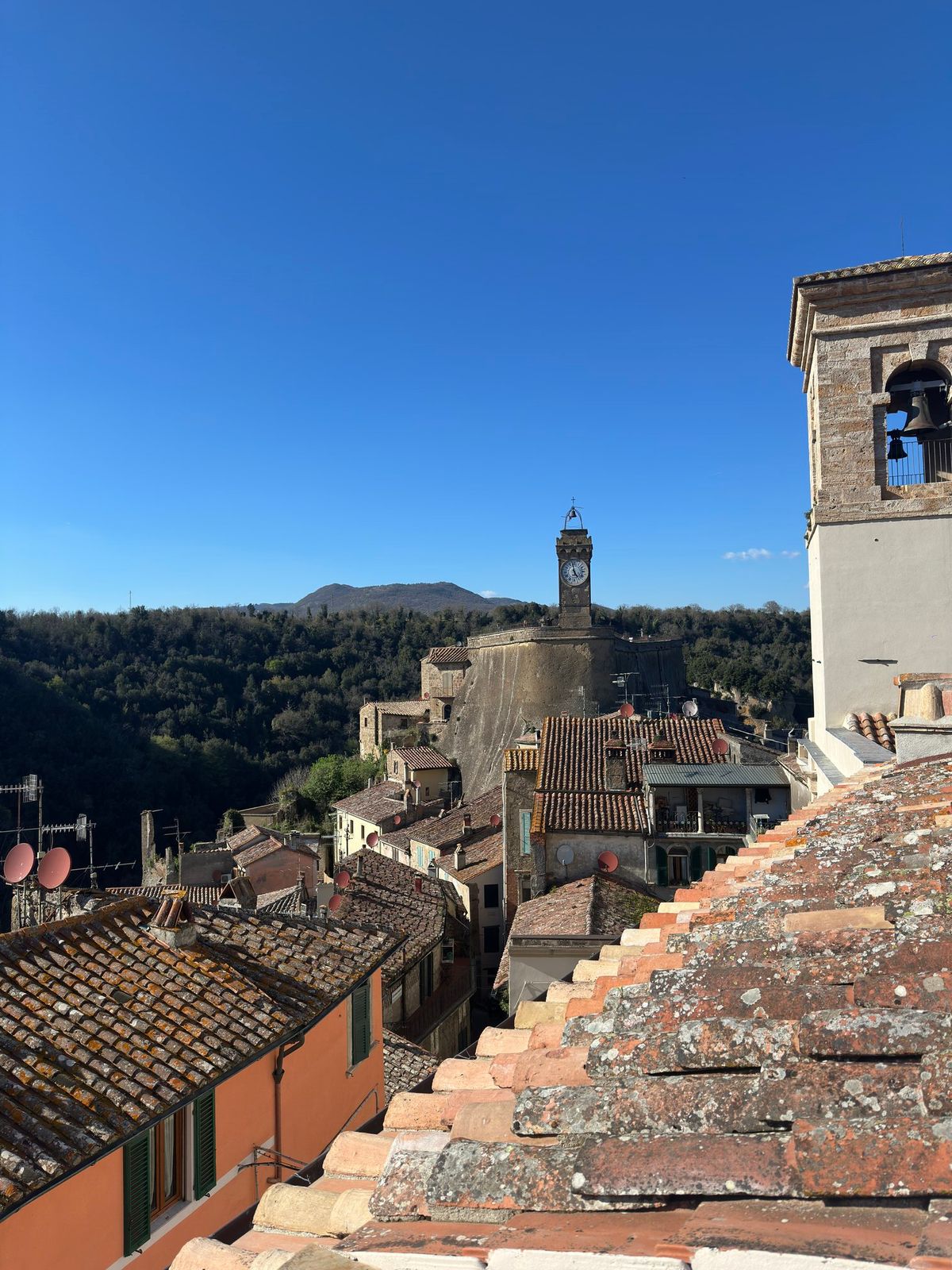 Sorano rooftops at dusk — terracotta tiles, the tuff cliff, distant Maremma valleys.