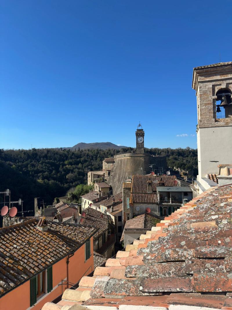 Sorano rooftops at dusk — terracotta tiles, the tuff cliff, distant Maremma valleys.