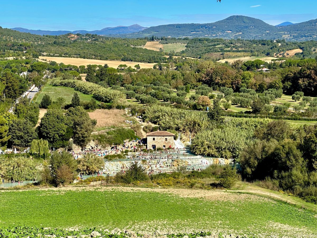 The Cascate del Mulino at Saturnia — travertine thermal pools and the historic mill, with bathers, above the Maremma countryside.