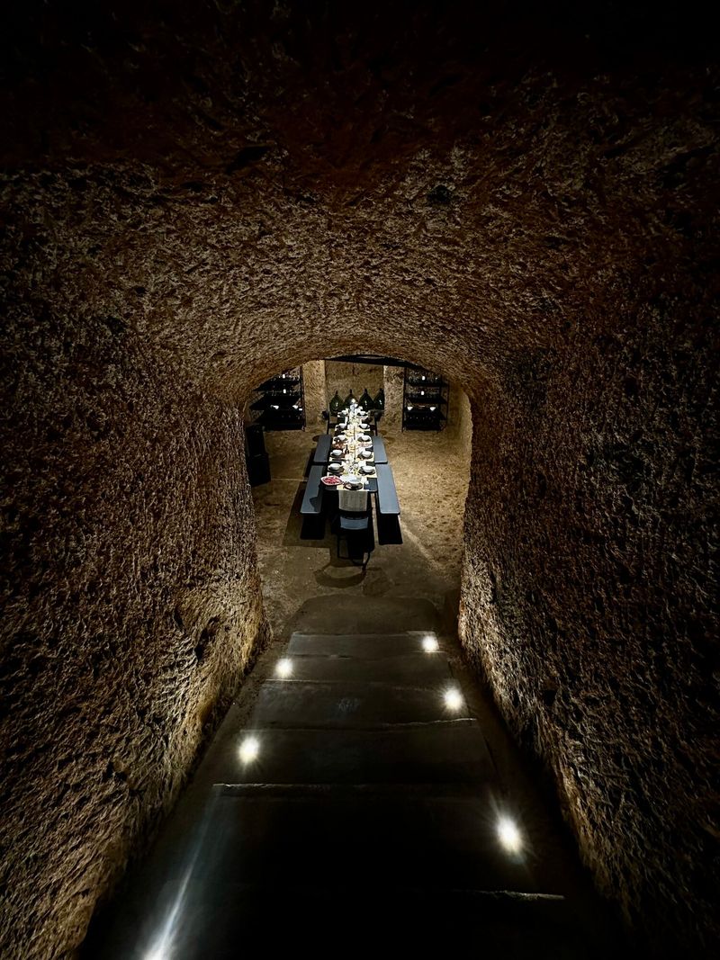 Cellar tunnel — arched tuff walls leading into candlelit darkness.