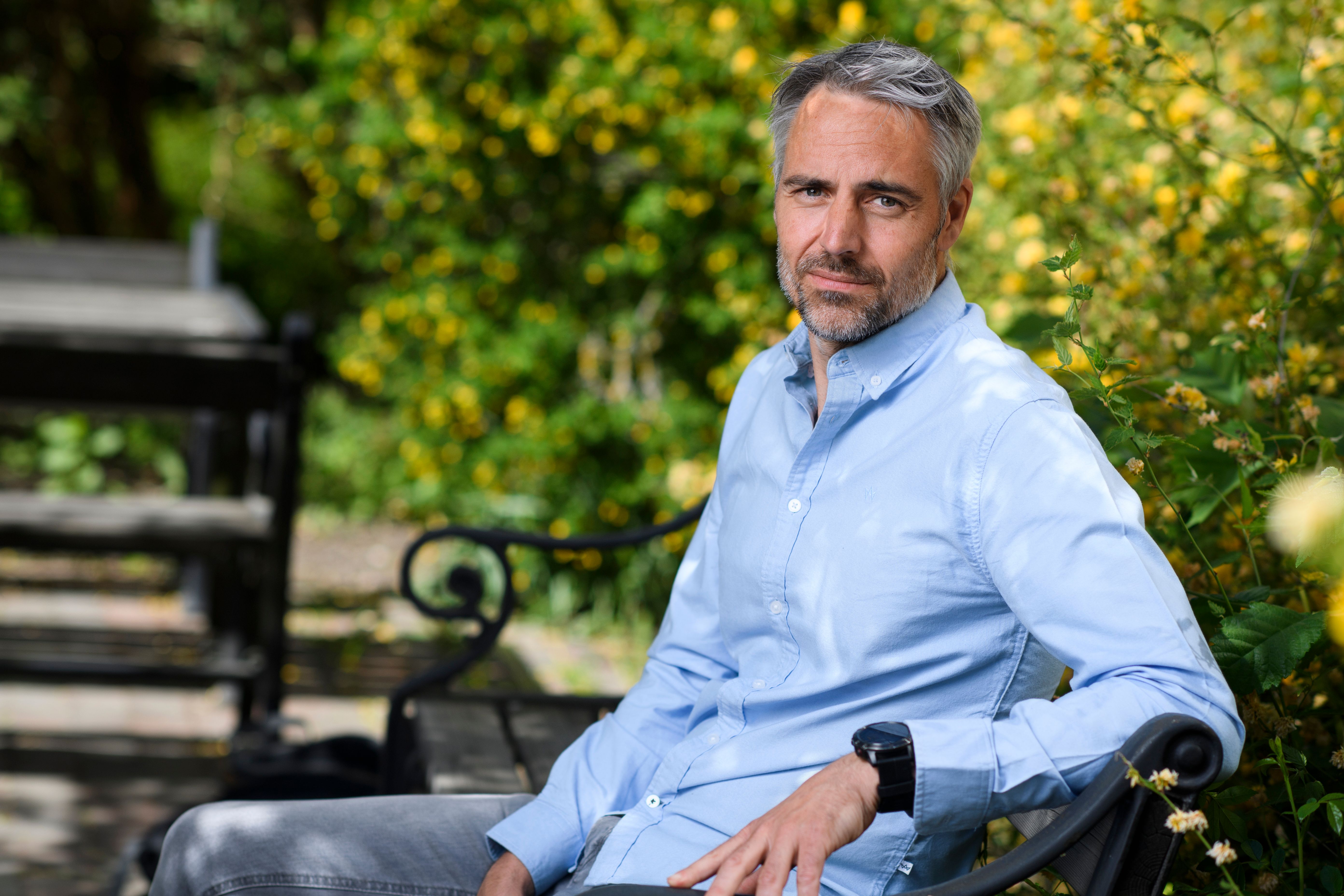 BYWRTRS kursledare, läkaren och författaren Anders Wallensten sitter i en park och ser in i kameran.