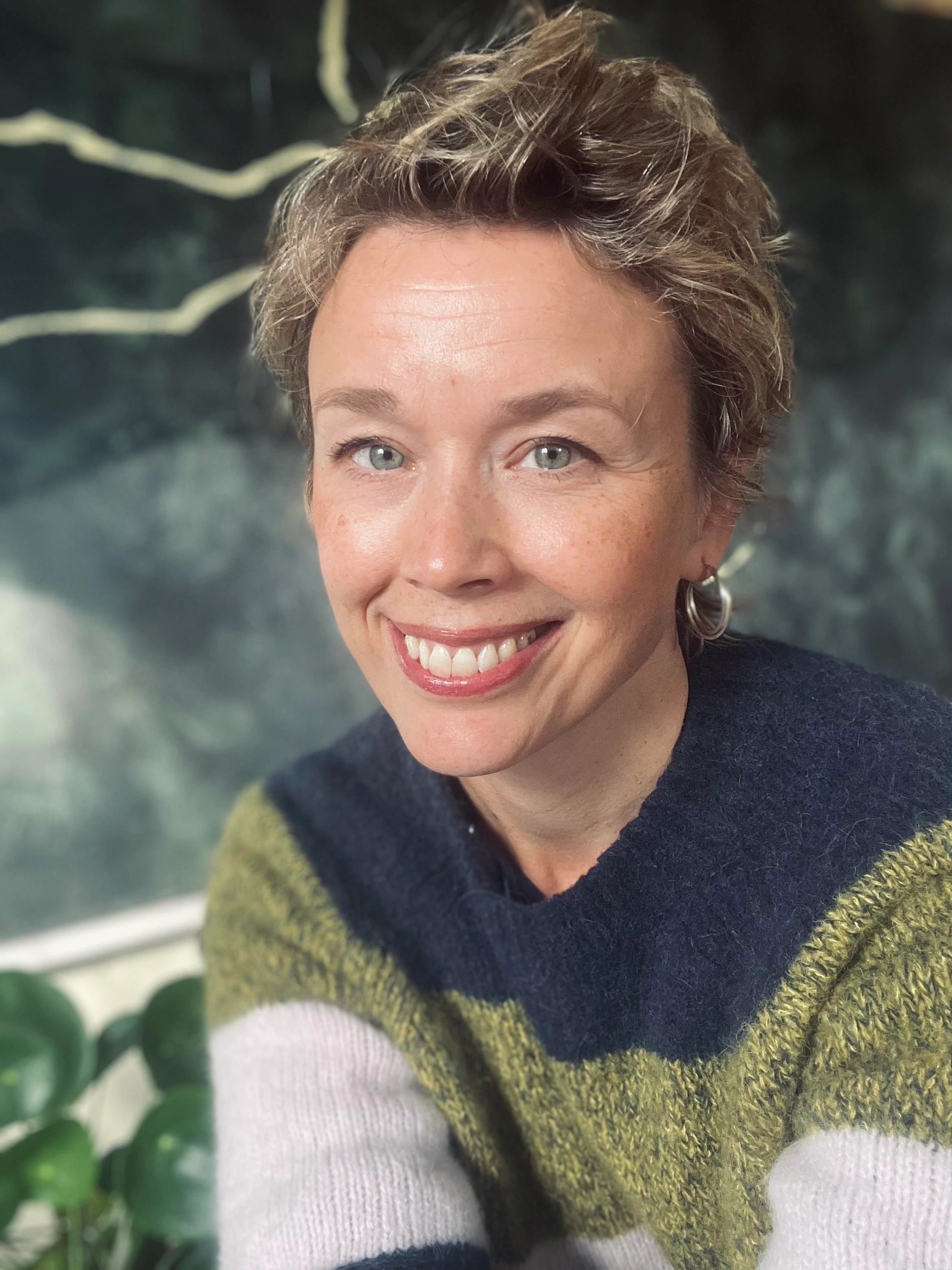 Leende Lisa Tallroth, Moderator och Programledare i flerfärgad stickad tröja mot naturbakgrund