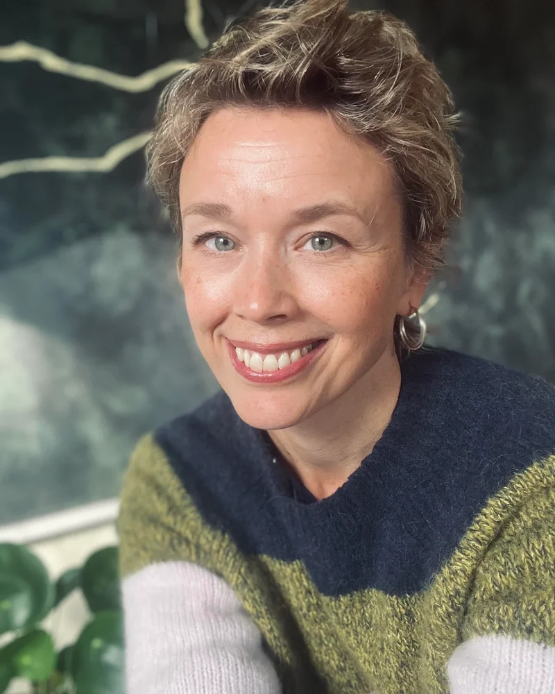 Leende Lisa Tallroth, Moderator och Programledare i flerfärgad stickad tröja mot naturbakgrund