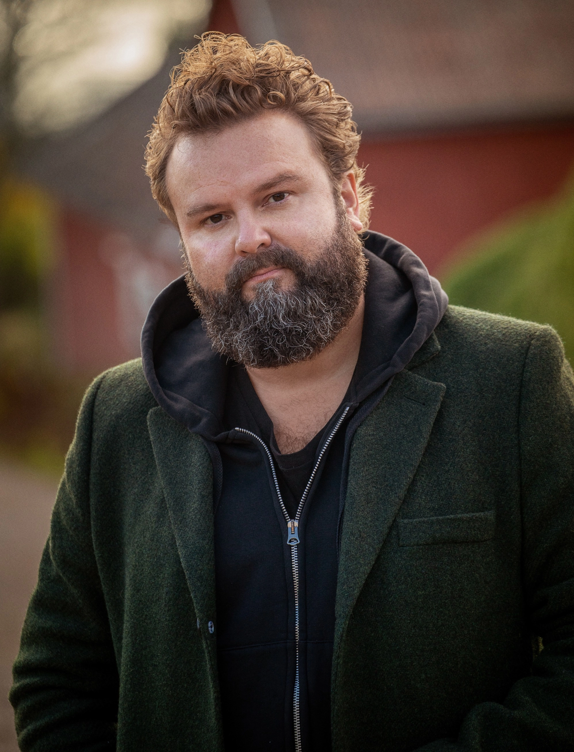 Niklas Turner Olovzon kollar in i kameran, han är en författare & Entréprenör i hoodie och mörkgrön kavaj 